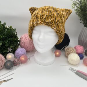 Getigerte Katzenohenmütze auf einem Styroporkopf. Im Hintergrund sind verschiedene Dekoelemente.