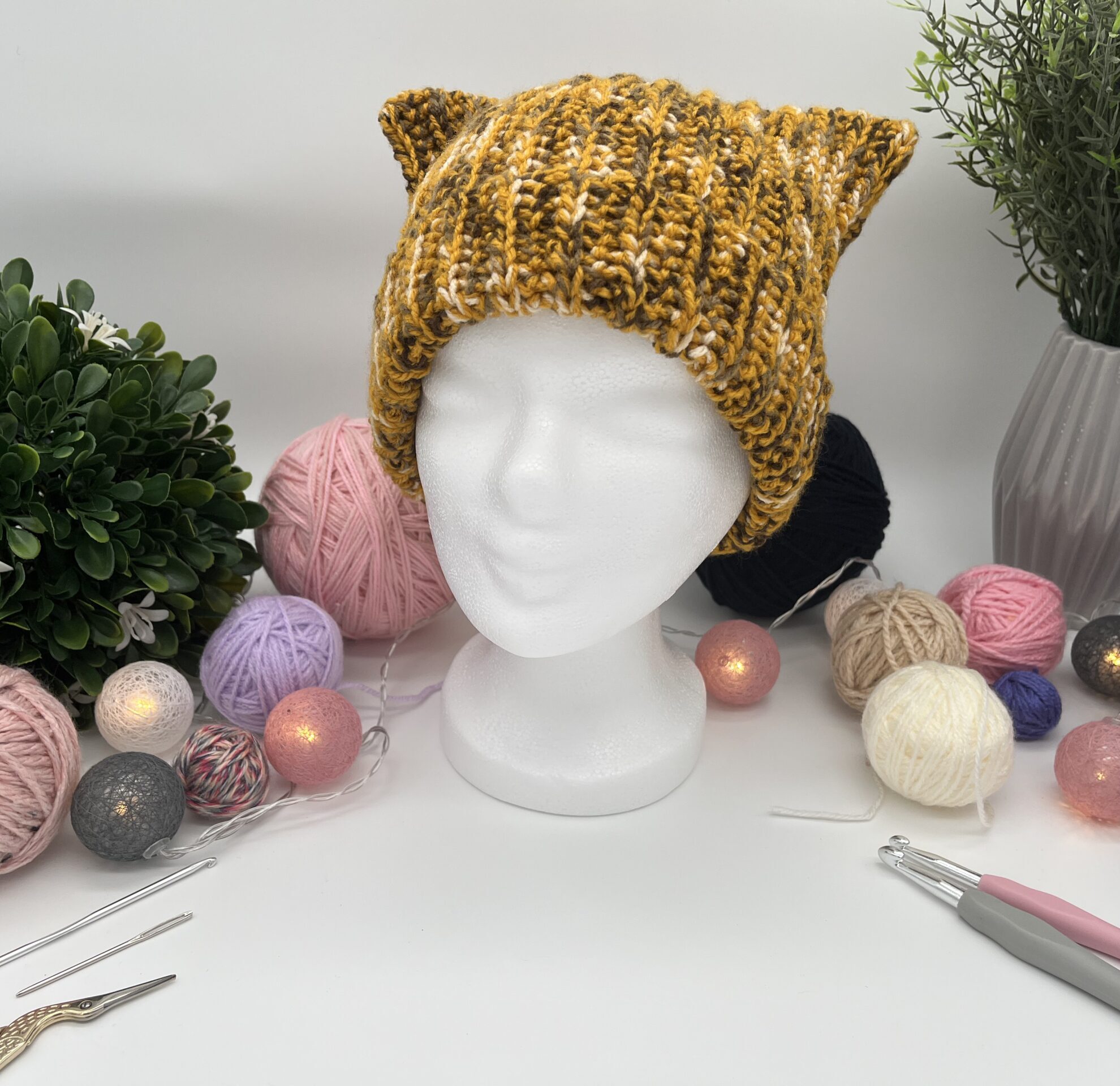 Getigerte Katzenohenmütze auf einem Styroporkopf. Im Hintergrund sind verschiedene Dekoelemente.