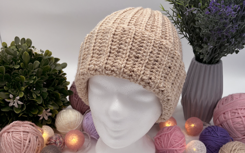 Beigefarbene Mütze auf Styroporkopf, dekoriert mit Wolle.