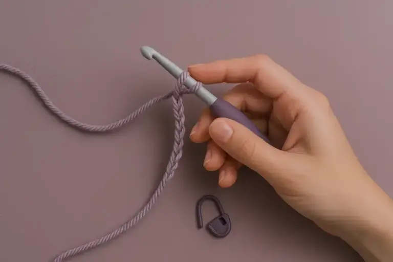 Hand hält Häkelnadel mit einer Luftmaschenkette in lilafarbener Wolle.