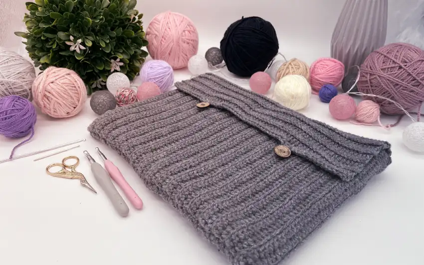 Laptophülle in Rosa und Grau mit Garnknäueln auf dekorativem Untergrund.