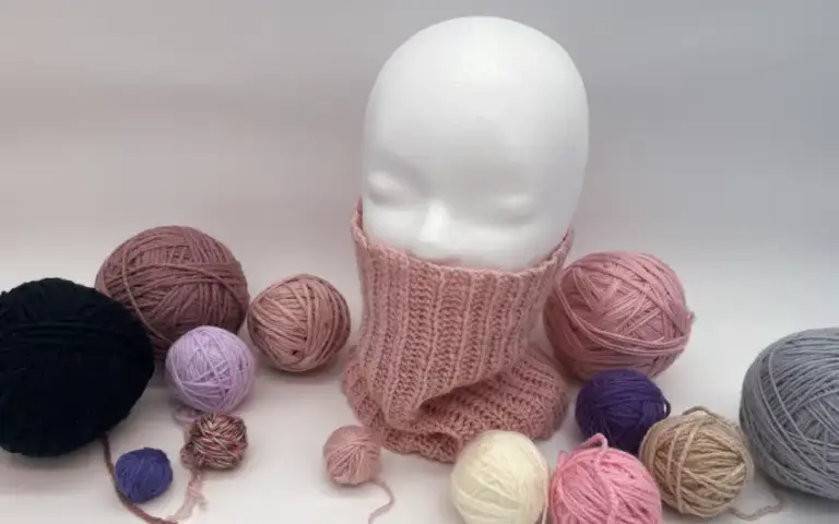 Styroporkopf trägt gehäkelten Loopschal mit Garn im Hintergrund.