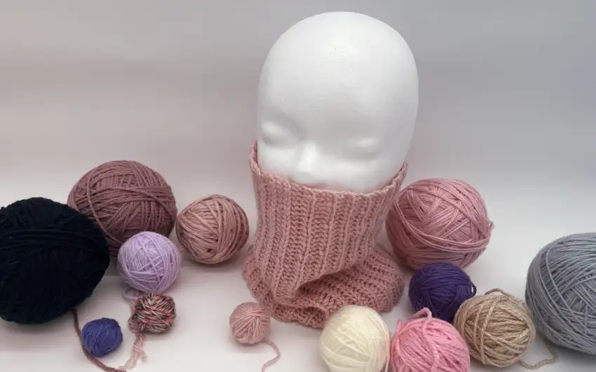 Styroporkopf trägt gehäkelten Loopschal mit Garn im Hintergrund.